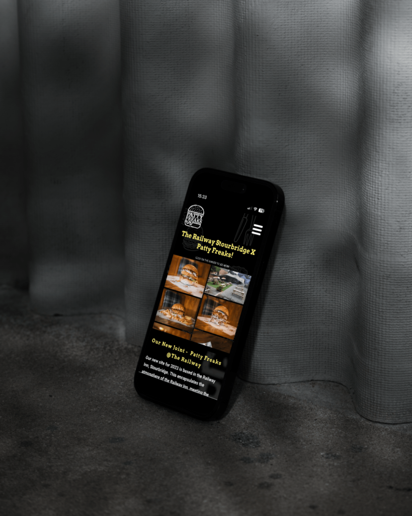 Mobile Phone with the Patty Freaks Restaurant Home Page displayed on a grey background 